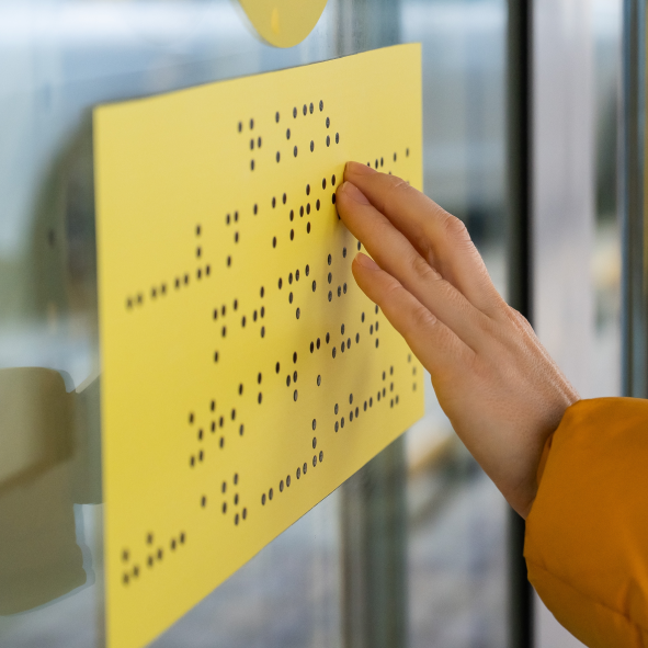 Zbliżenie na dłoń dotykającą żółtej tabliczki z tekstem w alfabecie braille'a