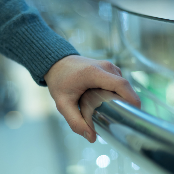 Zbliżenie na męską dłoń w centrum handlowym, która pewnie trzyma aluminiową poręcz.